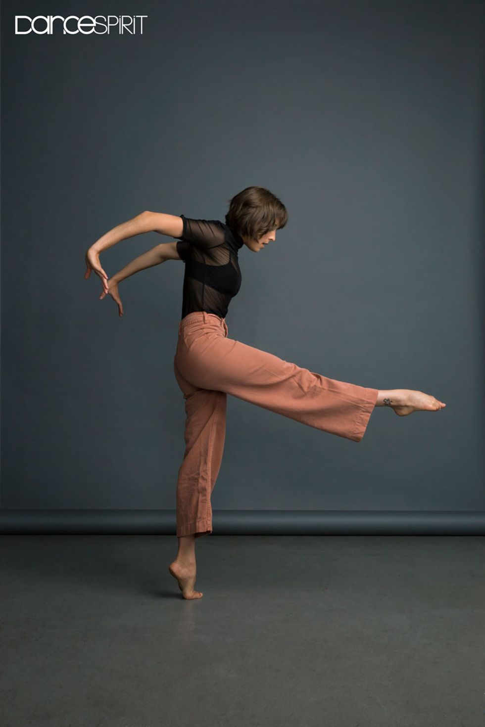Gianna Reisen - a young woman with brown hair in a bob - poses with her arms outstretched behind her, as if pushing against an invisible wall, and her right foot outstretched in front of her.