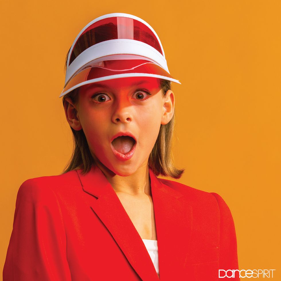 Eleven-year-old Gracyn French, wearing a bold red blazer, with a red and white vizor. There's an orange background, and she is looking at the camera with an expression of pleasant surprise.
