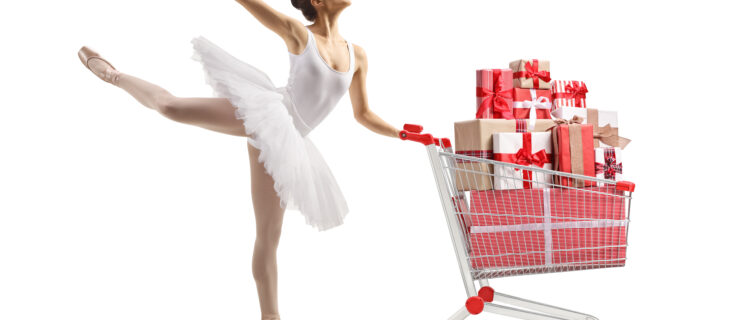 Ballerina dancing and holding a shopping cart with presents against white background