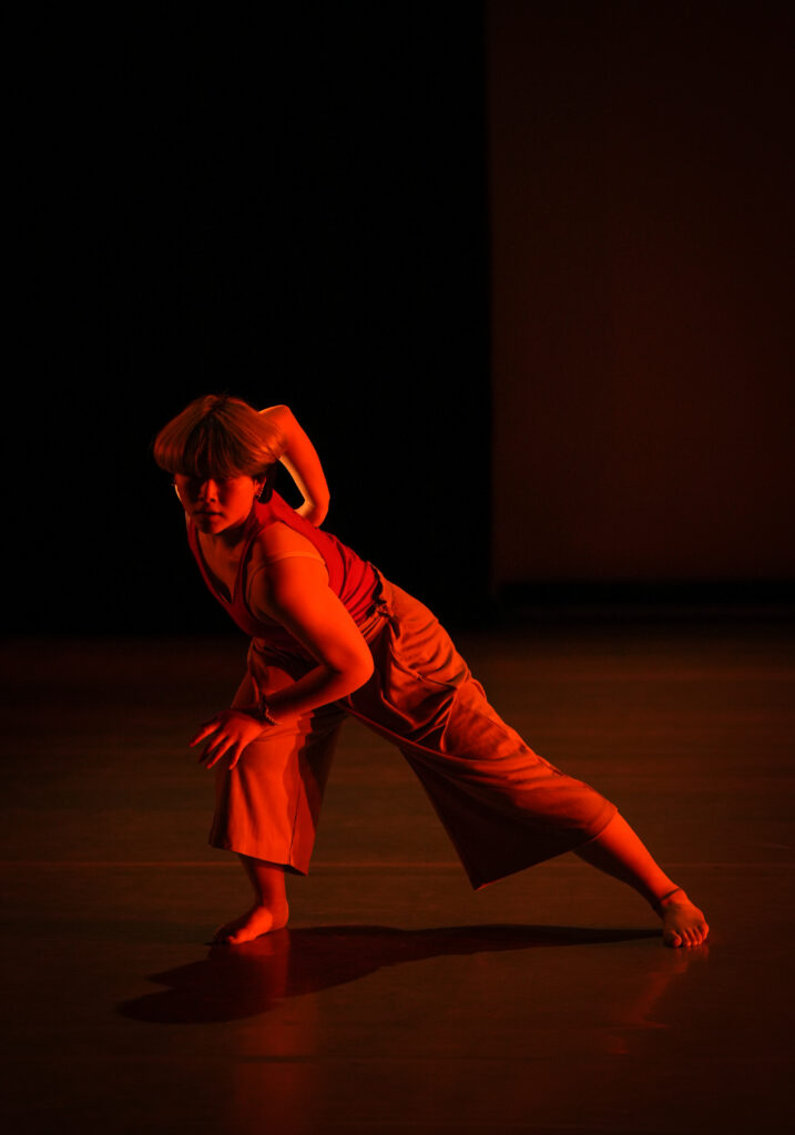 Zil Inami dancing on stage with harsh red lighting illuminating their movement 