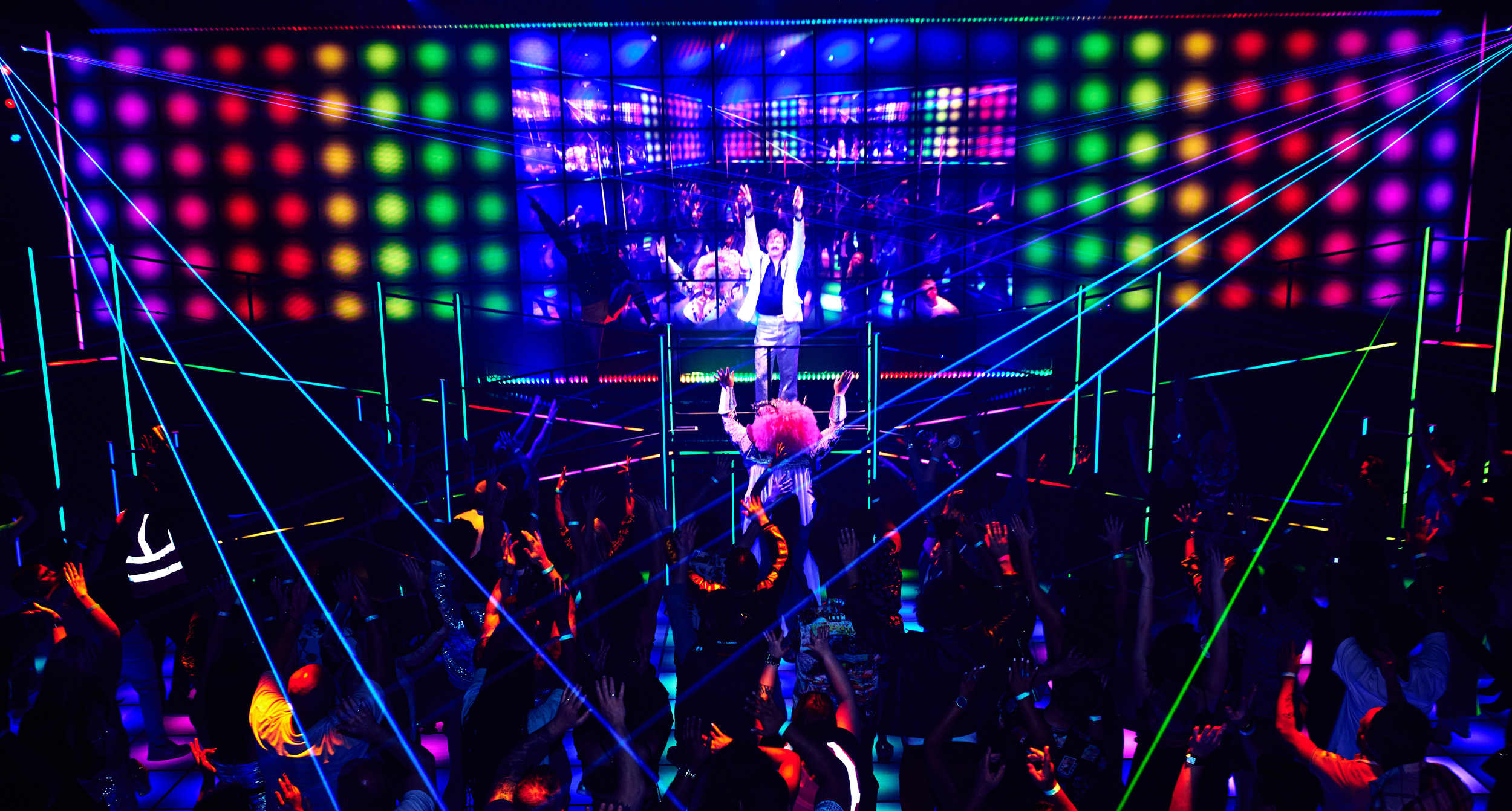 A large group of people dancing under neon lights shining all around.