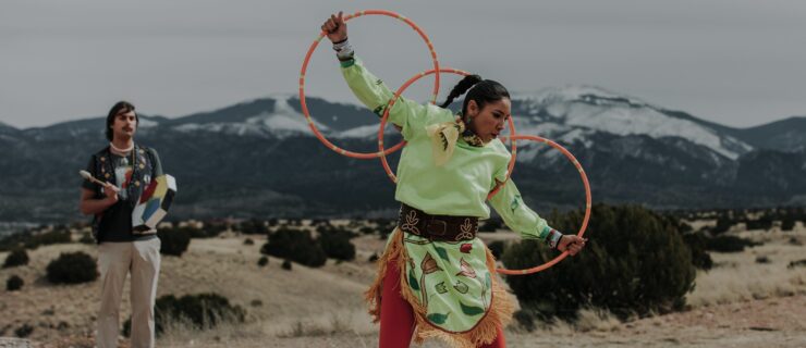 ShanDien Sonwai LaRance dancing outdoors in front of a large mountain with three orange hoops