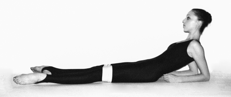 A dancer lying on back with her elbows propped under her. Her legs are turned out and a band is around her knees.