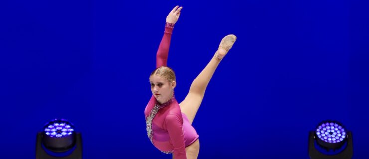 Margaret Jarvie dancing on stage wearing a long sleeved red leotard and performing an arabesque