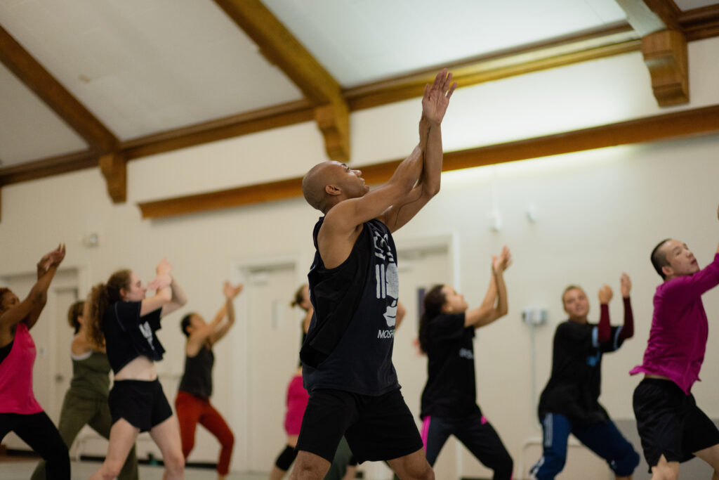 Shamel Pitts leads students in the studio by raising their arms and crossing them in front of them