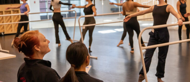 Jennifer Backhaus sitting at the front of the studio watching students perform barre exercises