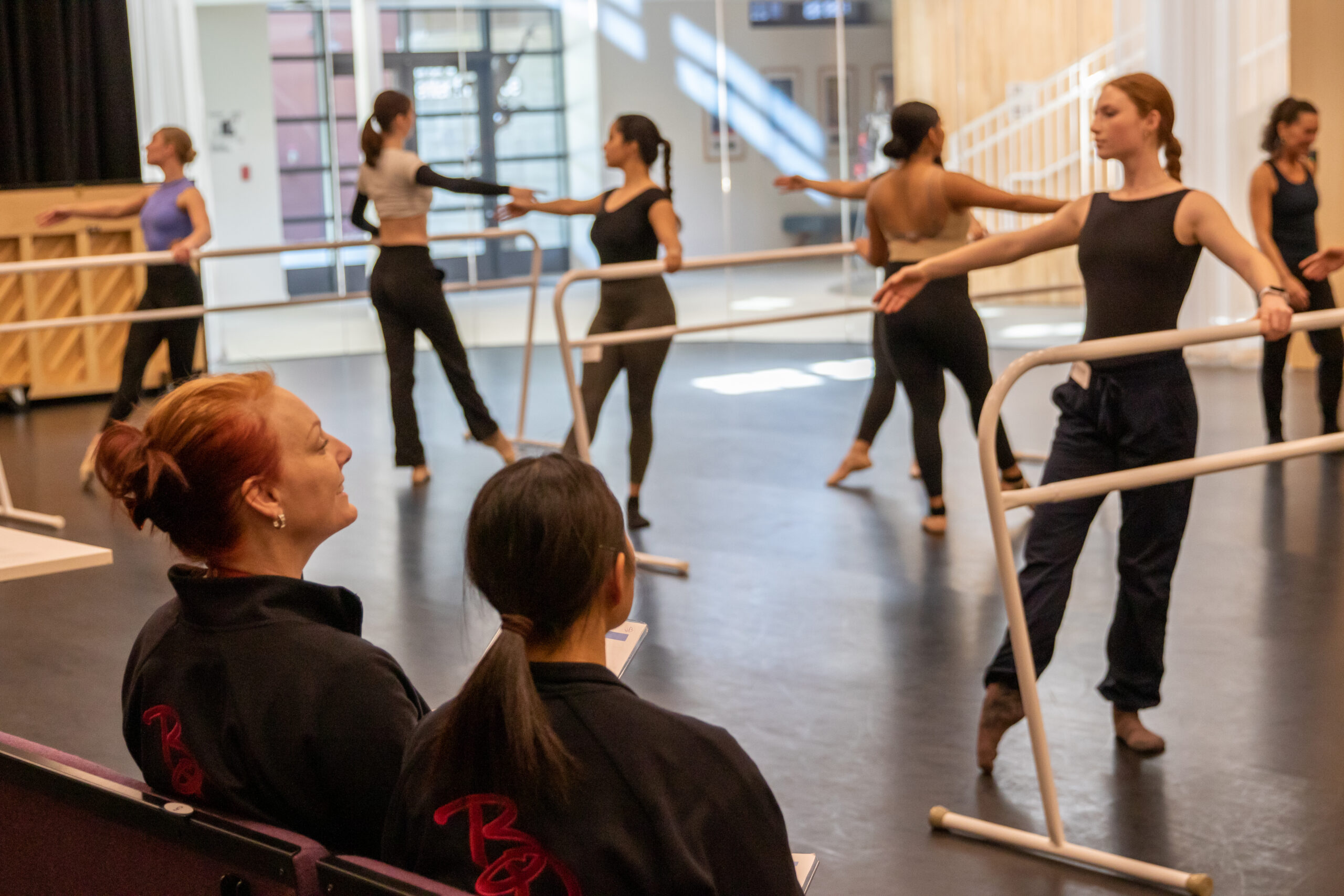 Jennifer Backhaus sitting at the front of the studio watching students perform barre exercises