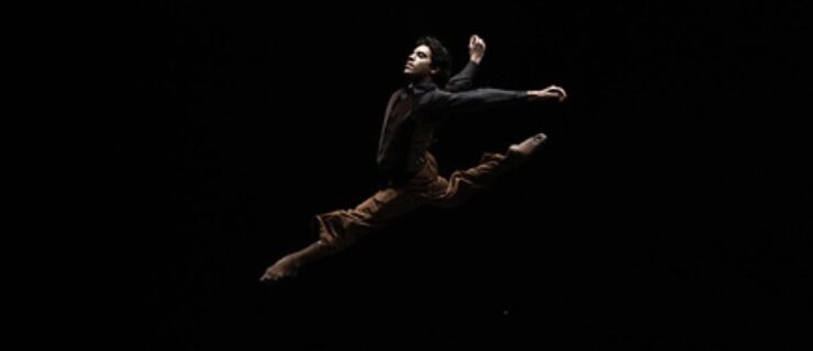 Alejandro Vargas performing a split in the air on a dimly lit stage