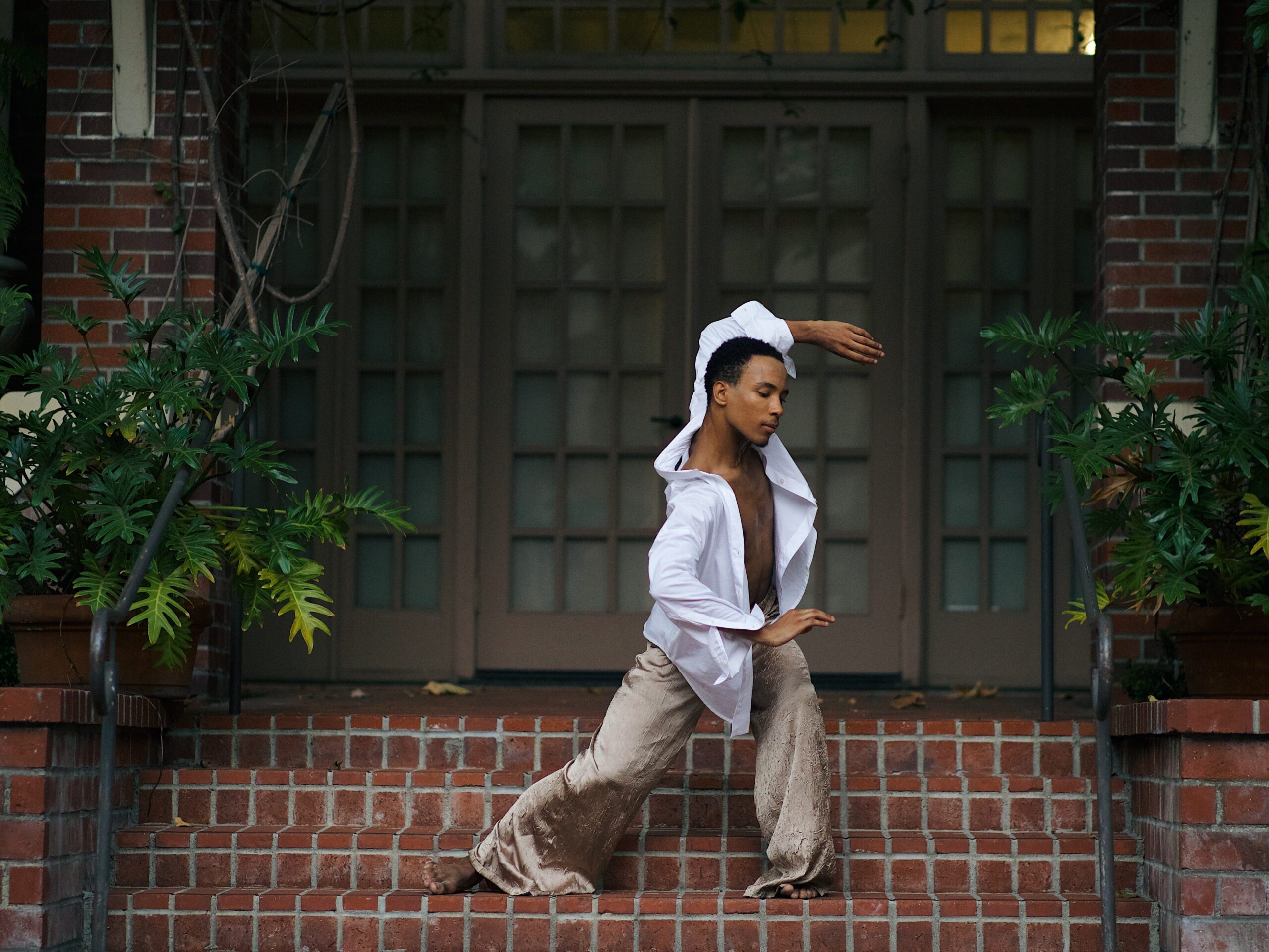 Browner dances on brick steps wearing a white button down and flowy tan pants 