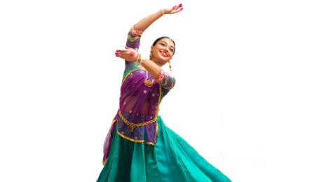 Radha Varadan lifting her arms while dancing in a colorful traditional dress.
