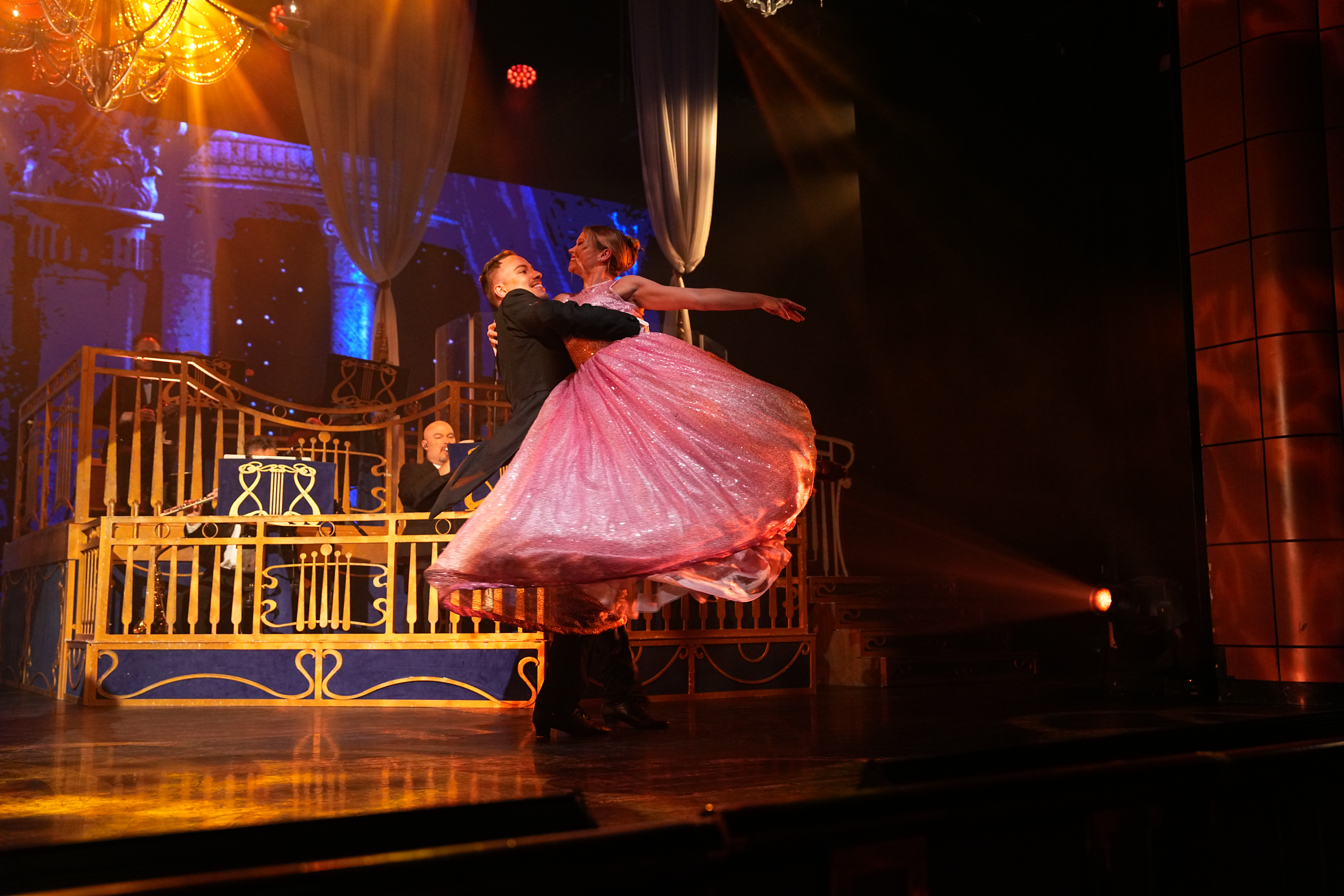 Amanda Sherwin wears a pink ball gown and is lifted in the air by a supporting dancer.