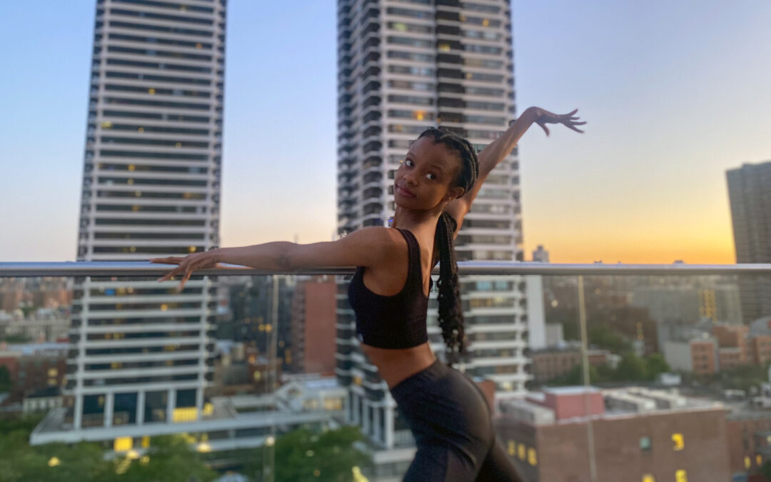 Murray—a Black woman wearing a black crop top and black pants, her long braids pulled into a low ponytail—poses on a city rooftop. Her left arm drapes elegantly over the railing as she extends her right arm up and out behind her.