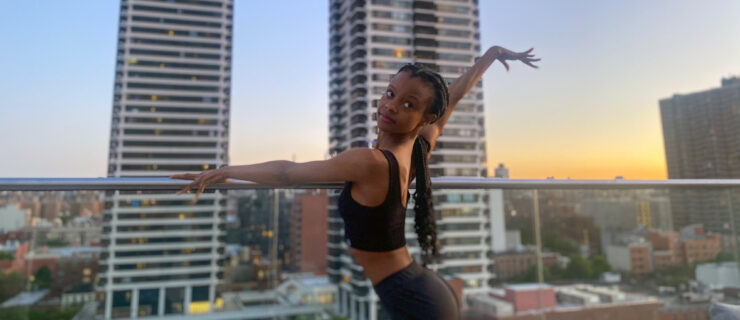 Murray—a Black woman wearing a black crop top and black pants, her long braids pulled into a low ponytail—poses on a city rooftop. Her left arm drapes elegantly over the railing as she extends her right arm up and out behind her.