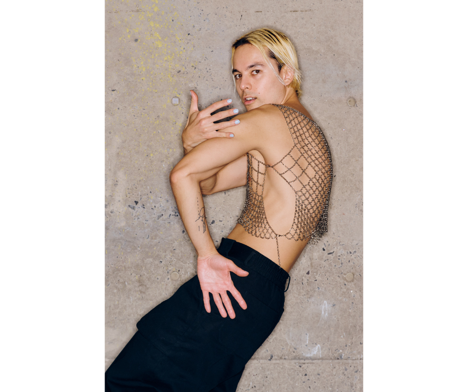 Akira Uchida contracting, with his arms wrapping in front. He wears a chain link top and black pants.