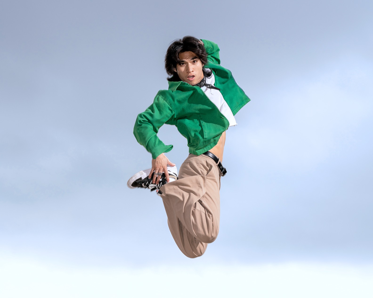 Gabe De Guzman wearing a green shirt and tan pants. He jumps in the air with his legs bent.