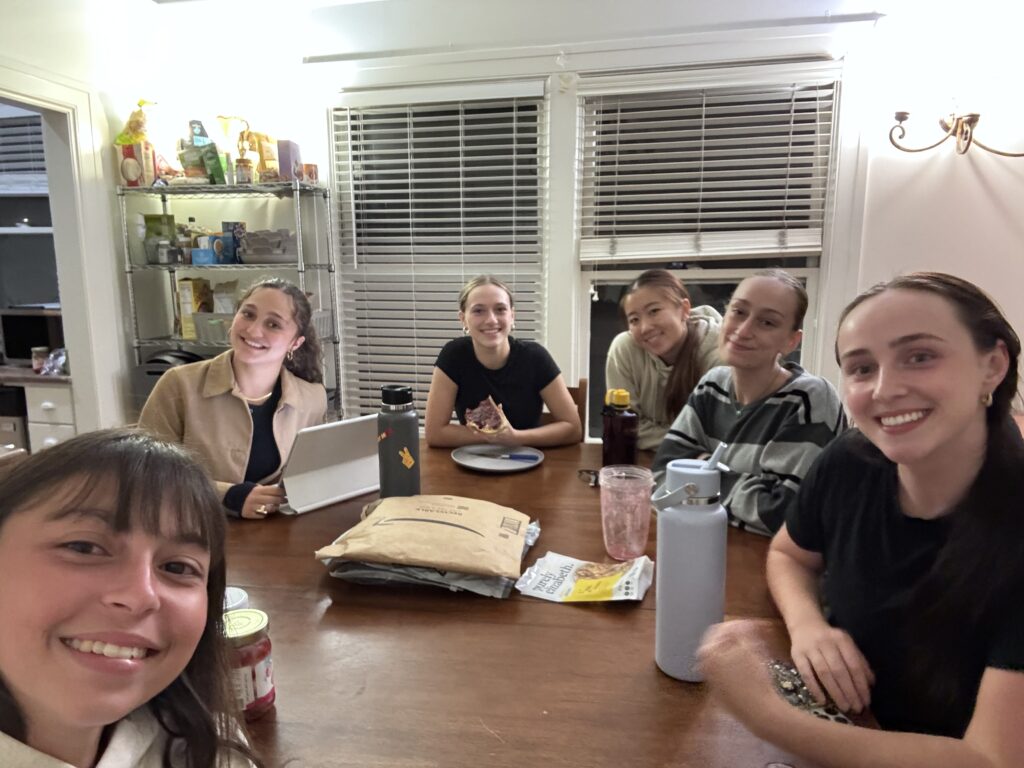 A group of college roommates smile for a photo as they sit around a kitchen table.