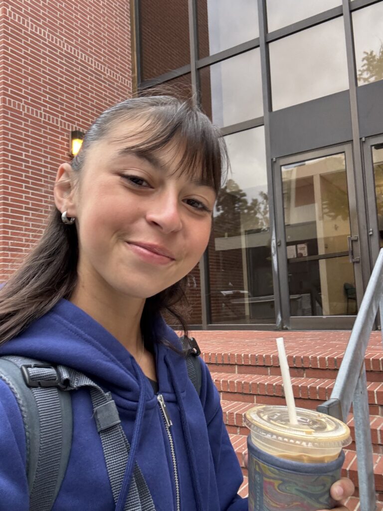 Katie Tapalaga poses with an iced coffee outside of a college building.