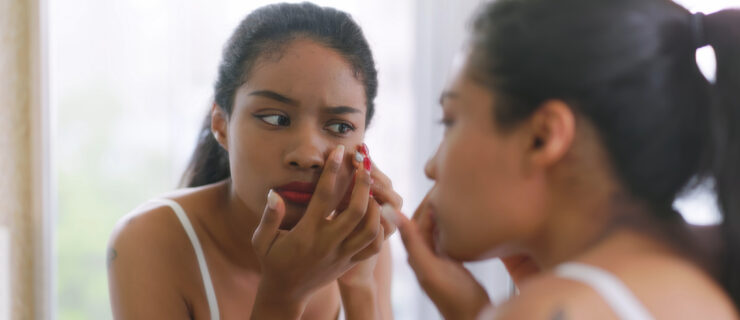 A close-up shot of a young woman looking at her reflection in the mirror. She is upset because she has a pimple.