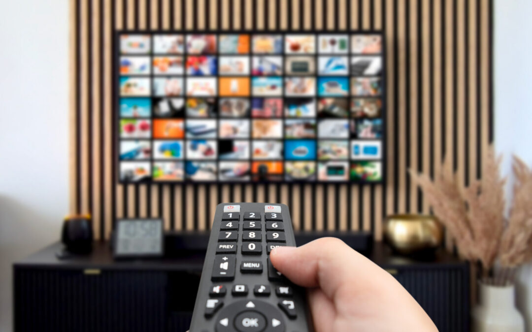 A close-up shot of someone's hand holding a TV remote, pointed toward the screen on the opposite wall.