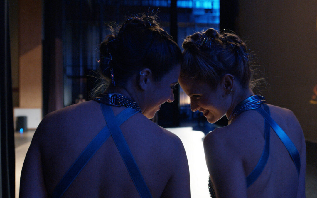 A close-up of Mackenzie Ziegler and Audrey Zahn backstage at a dance competition, in costume, laughing and touching their foreheads together.