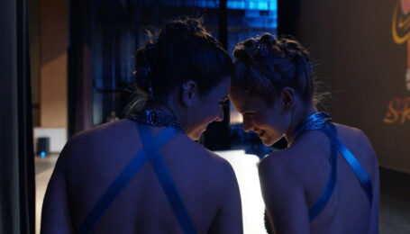 A close-up of Mackenzie Ziegler and Audrey Zahn backstage at a dance competition, in costume, laughing and touching their foreheads together.