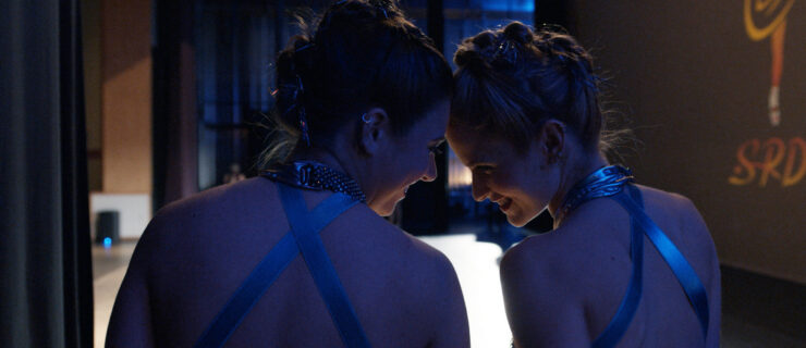 A close-up of Mackenzie Ziegler and Audrey Zahn backstage at a dance competition, in costume, laughing and touching their foreheads together.