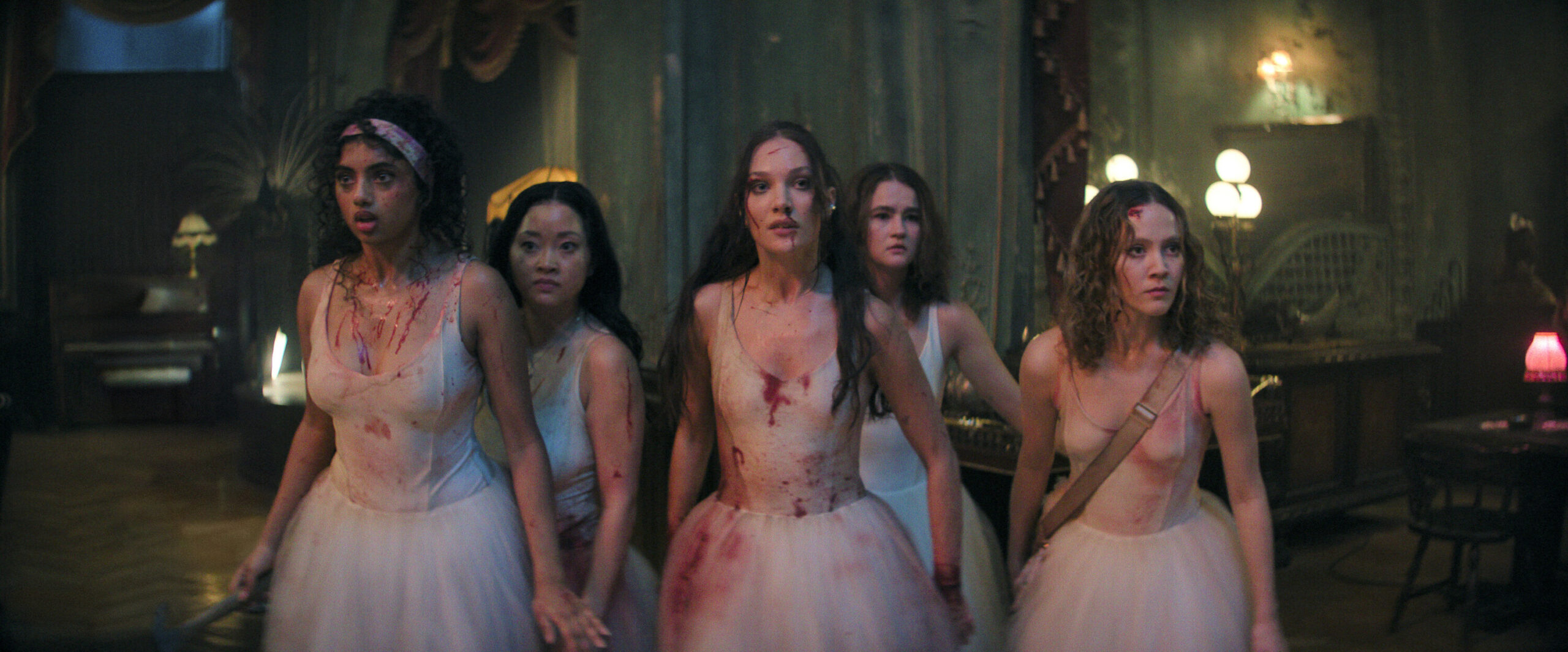 Five teenage ballerinas, wearing bloodstained white Romantic tutus, stand together in a dingy inn lobby with alarmed, but focused, expressions.