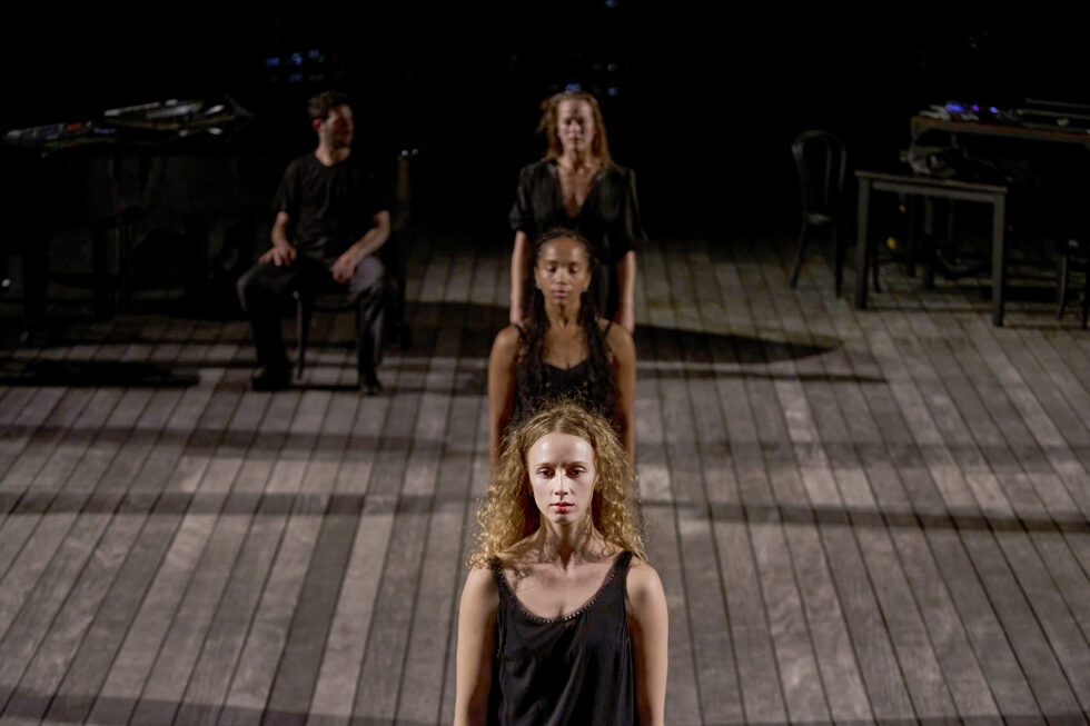 Johnson and other performers make a vertical line on stage. They stare forward with their arms by their sides. 