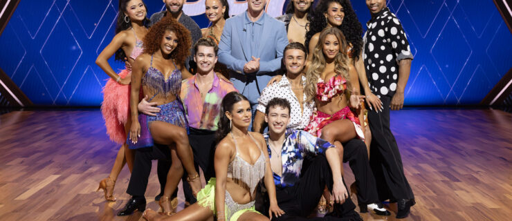 A group of dancers in various ballroom and Latin dance costumes pose for a group photo surrounding Robert Irwin, who wears a powder-blue suit.
