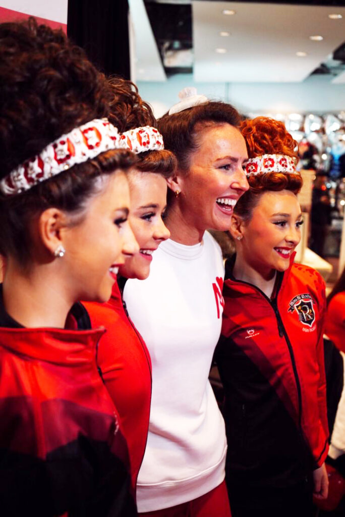 Three Irish dancers and a coach huddle together for a group photo.