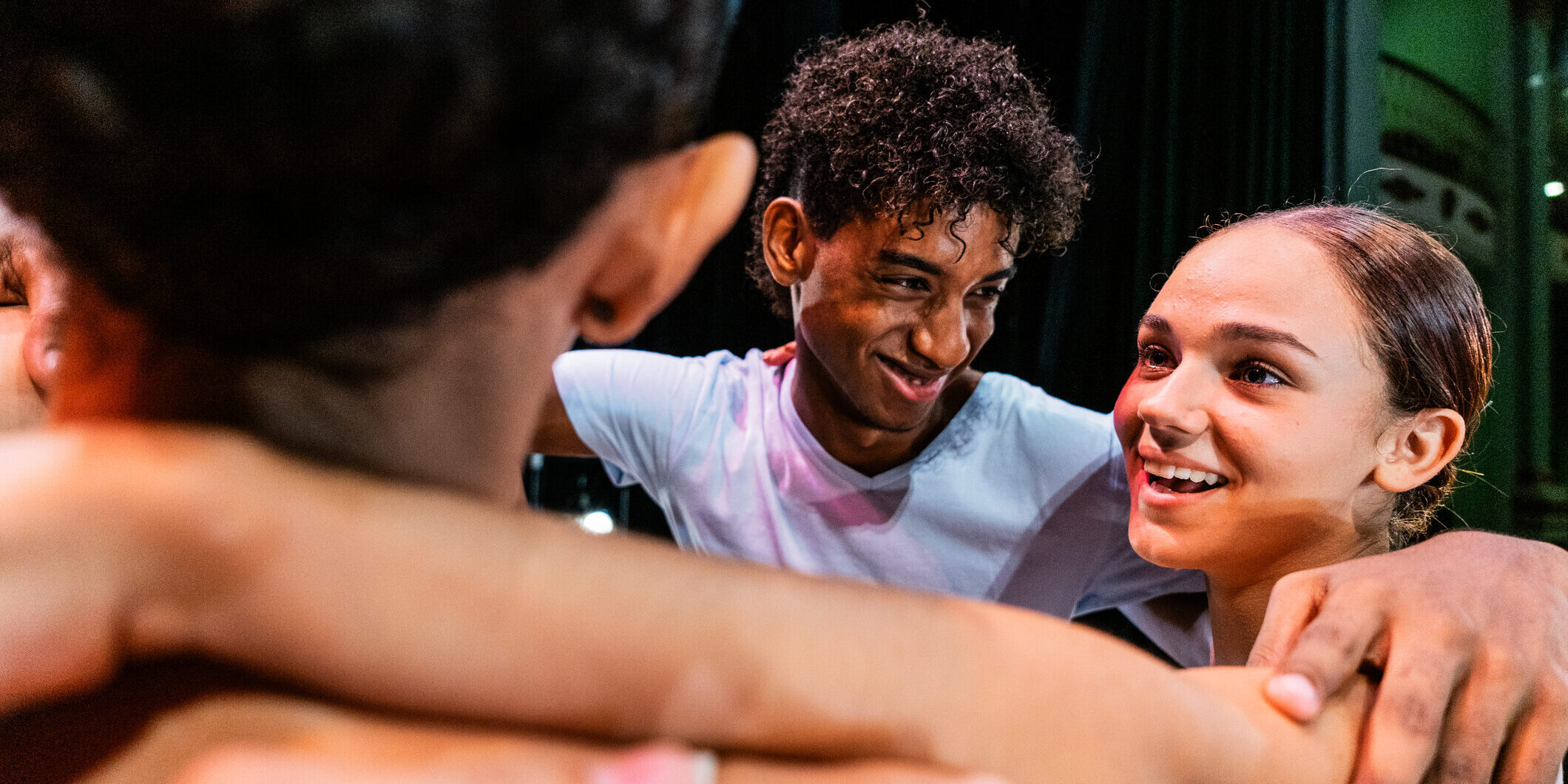 A group of teenage dancers huddle for a group hug onstage.