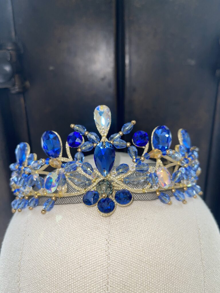A costume tiara with dark and light blue jewels, resting on a model head.