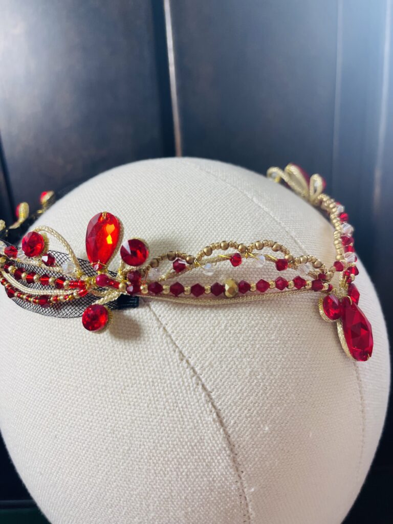 A red and gold ballet costume headpiece with a large red gem to adorn the forehead.