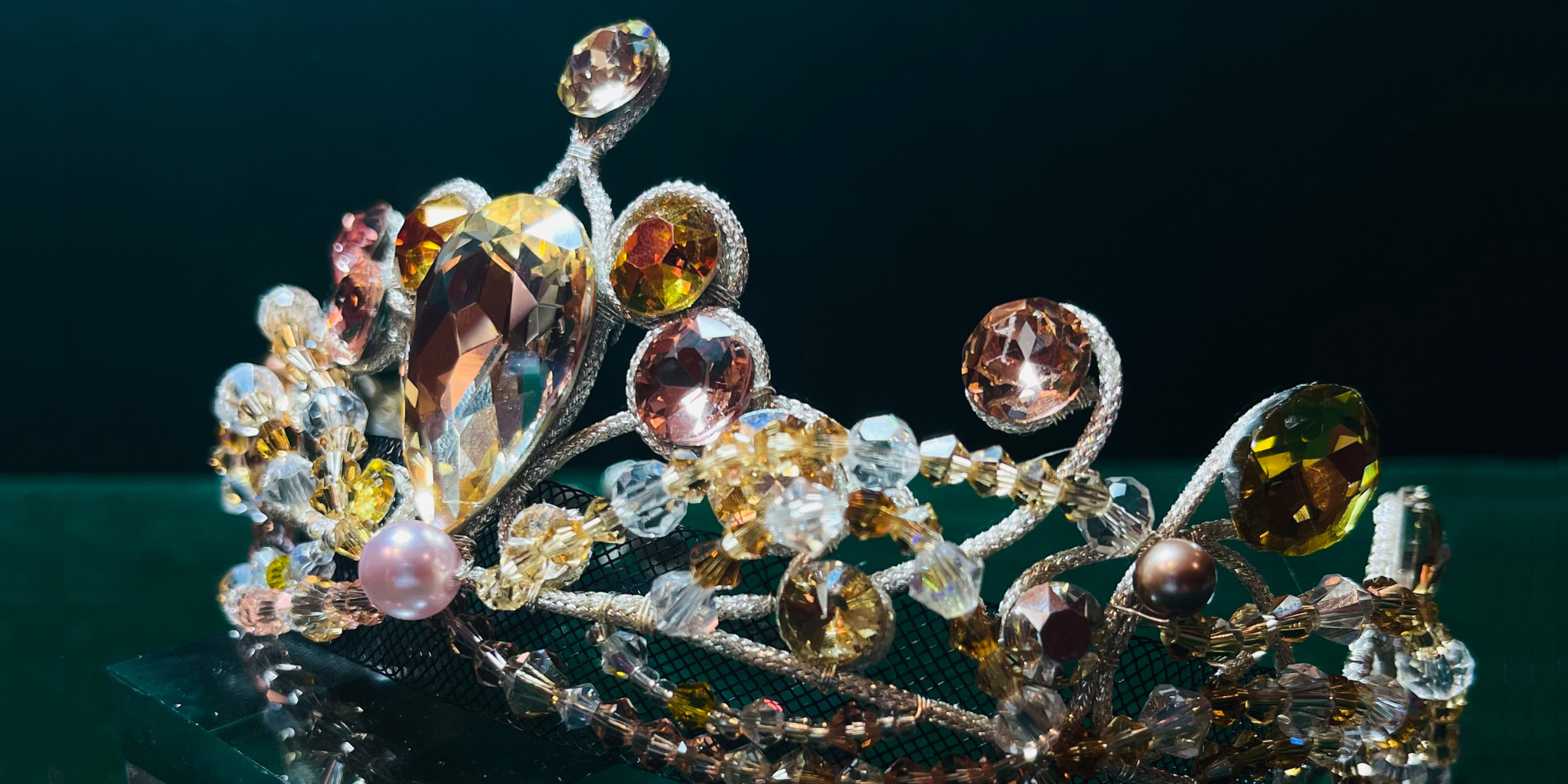 A close-up of a ballet costume tiara with white, amber, and light pink gems.