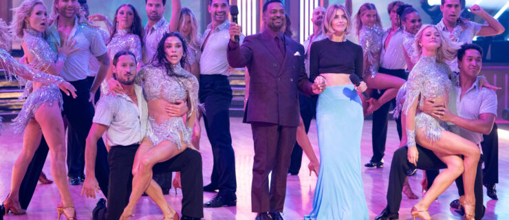 On the "DWTS" stage, a group of pros and troupe dancers in sparkly silver costumes pose around Alfonso Ribeiro and Julianne Hough, who hold microphones. The dancers' hair flips as they hit their final pose after an intense dance.