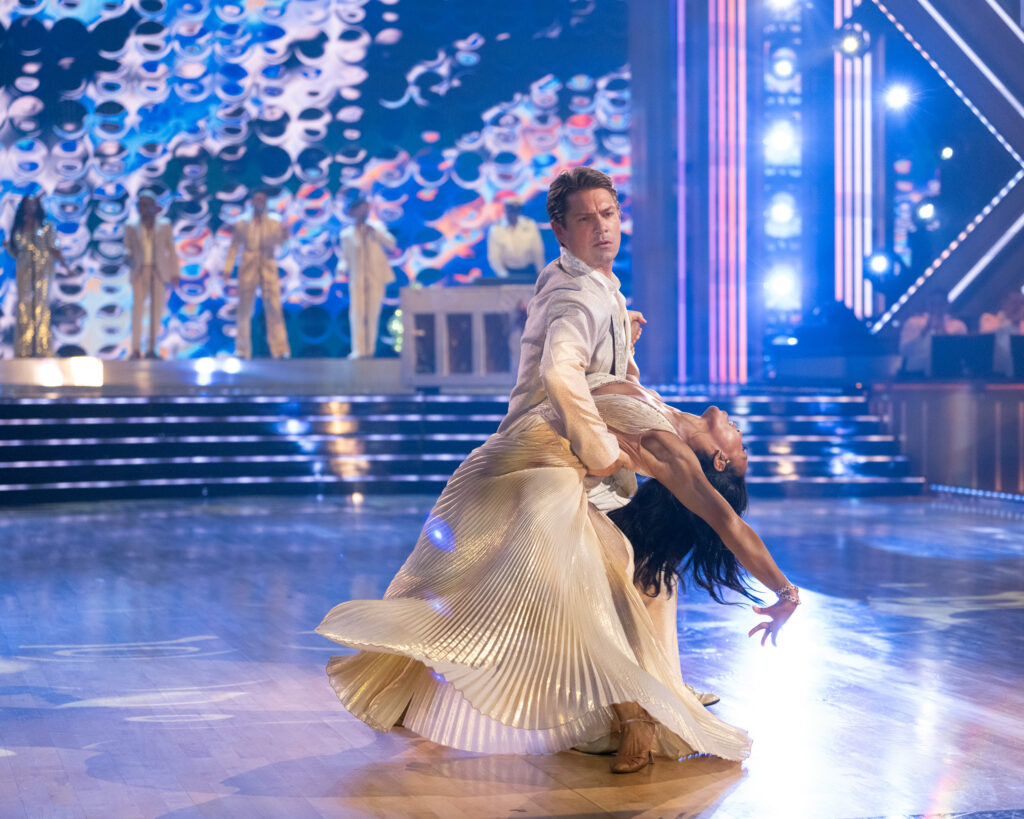 Taylor Hanson holds Britt Stewart in front of him, around her waist, as she dips back with one arm extended above her head and toward the floor. Her skirt swirls.