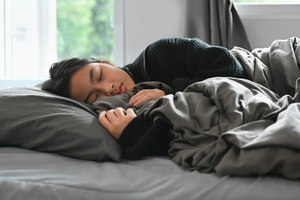 A teenager takes a nap in bed during daylight.