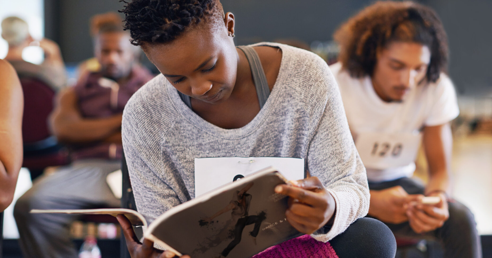 Shot of a young female dancer reading a dance magazine in a classroom.