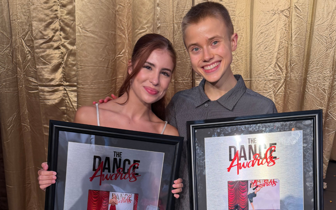 Cameron Voorhees and Ian Stegeman pose together in formal attire holding their respective dance awards. Behind them is a shimmery gold curtain.
