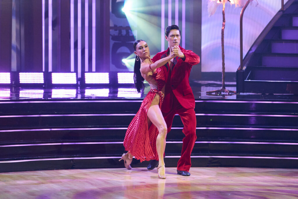 Jenna Johnson and Harry Shum Jr. step forward in a tango frame, their back legs extended as they look ahead with intense gazes.
