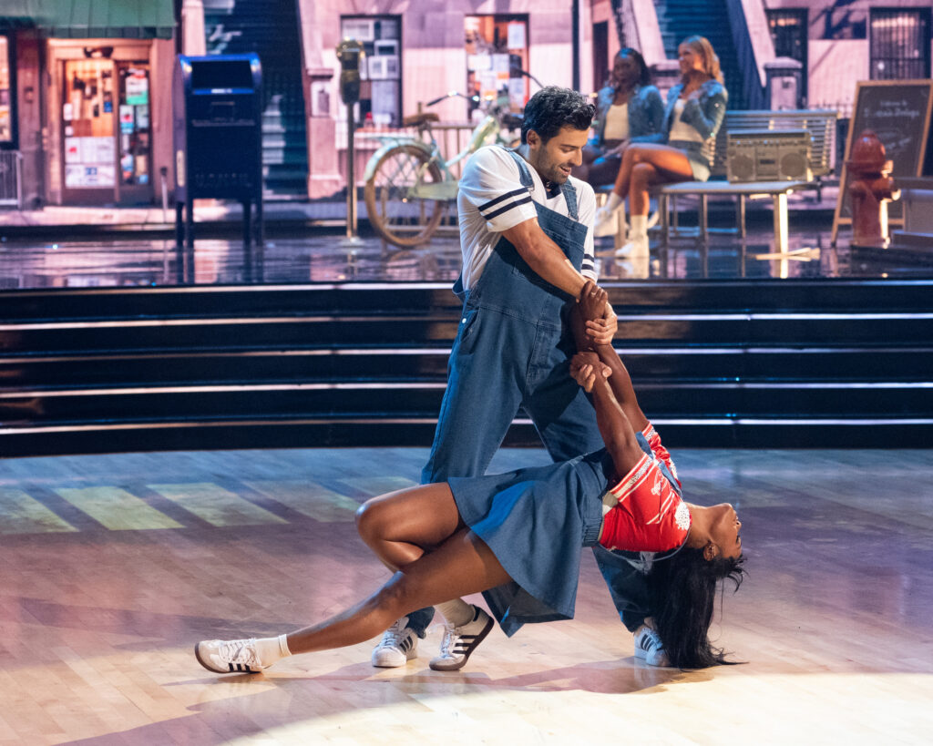 Jan Ravnik stands wide-legged and holds Tatyana Ali's arms as she leans back, one leg bent and the other long, so her head nearly touches the floor.