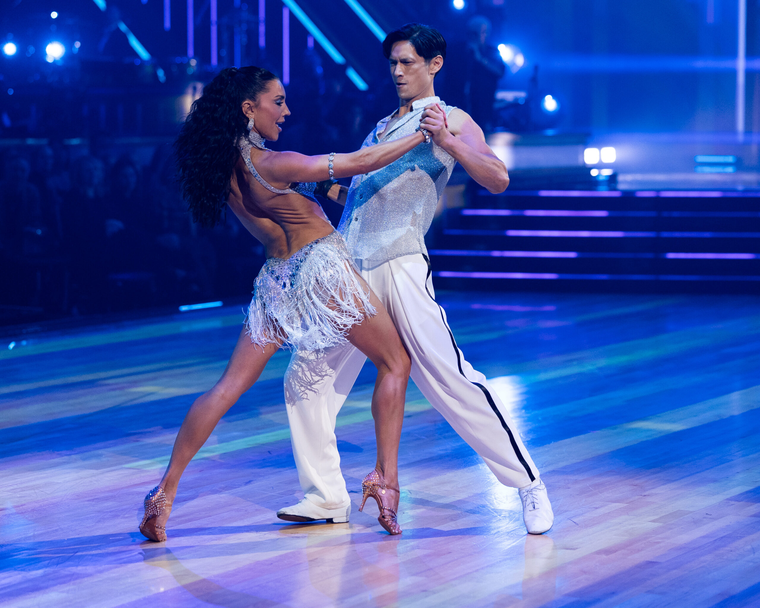Jenna Johnson and Harry Shum Jr. face each other and hold hands, hips forward toward each other with their back legs long and on demi pointe. They lean away with their upper bodies.