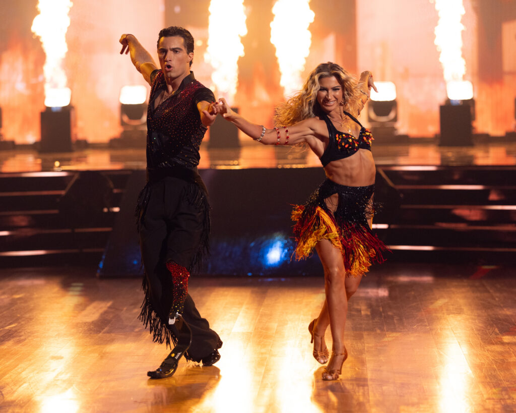 Ezra Frech and Daniella Karagach do a New Yorker to the front, their front hands held forward and their outside arms extended backward, as they cross one leg over and take a step forward.