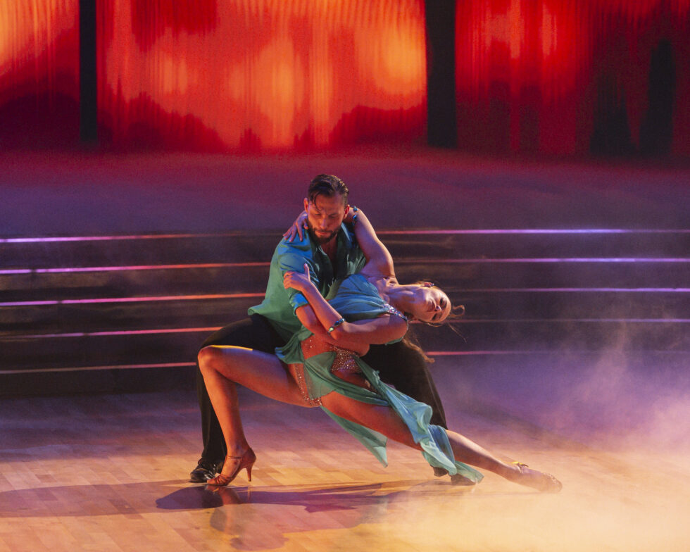 Allen Genken crouches and holds Adele Zaikman around the waist as she does a deep lunge, leaning backward with an arm around Genkin's shoulders.