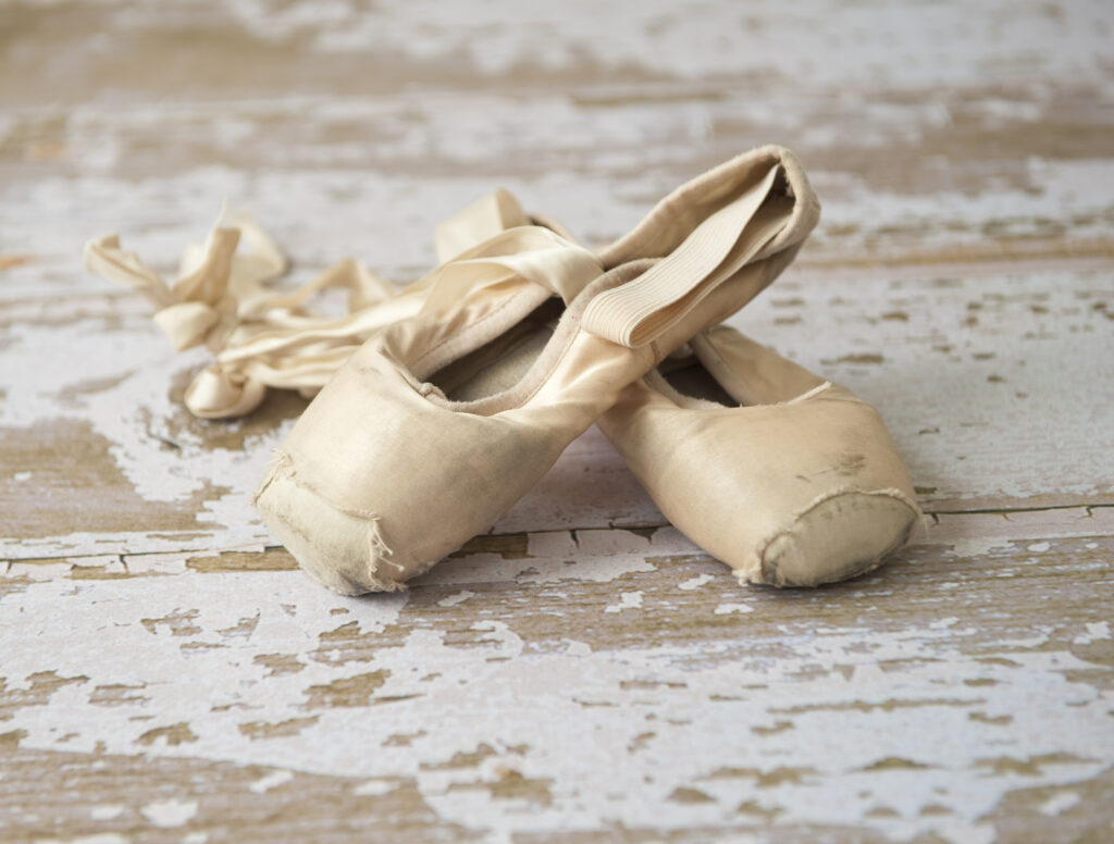 Old, worn out pointe shoes on a wooden floor.