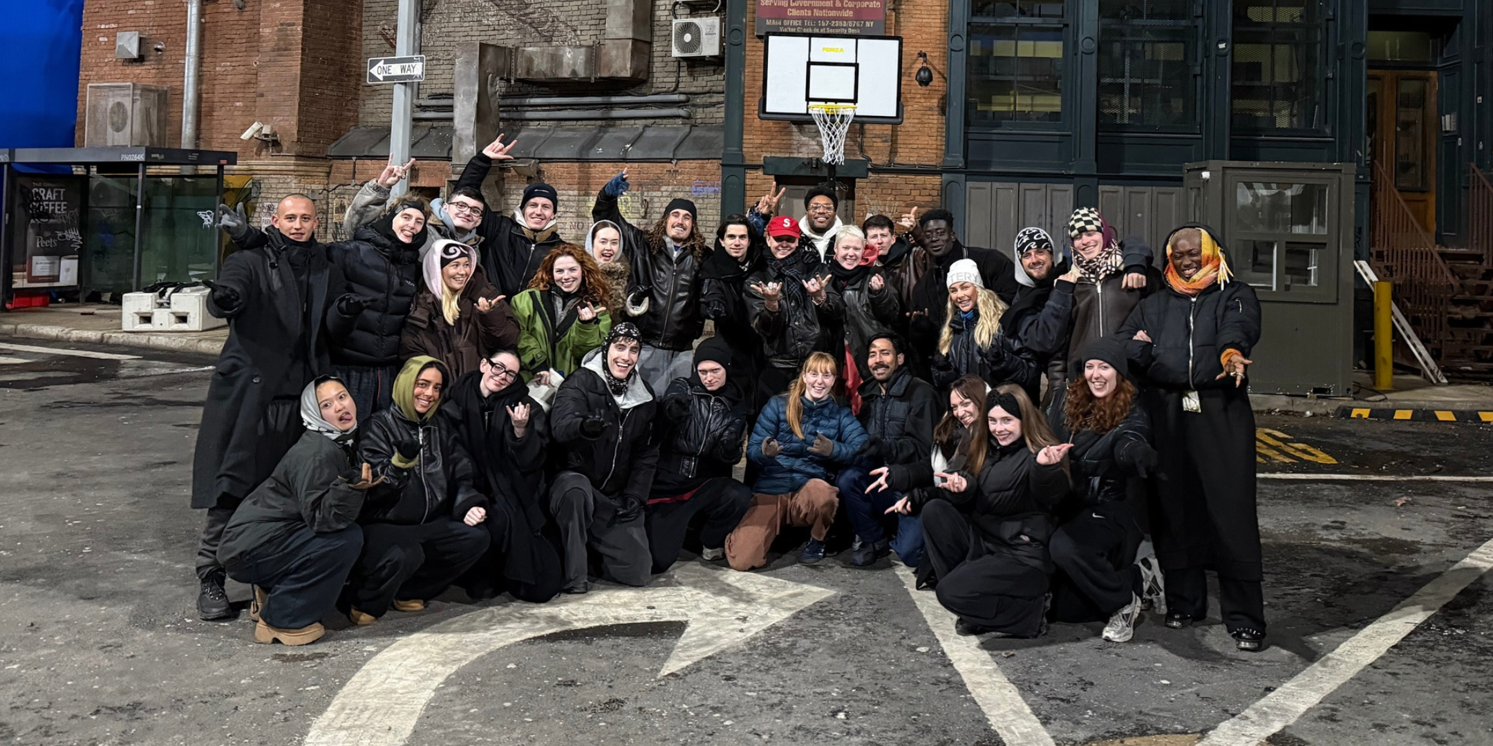 On the street at night, a large group of dancers pose together for a photo. They are bundled warmly with coats, hats, and scarves.
