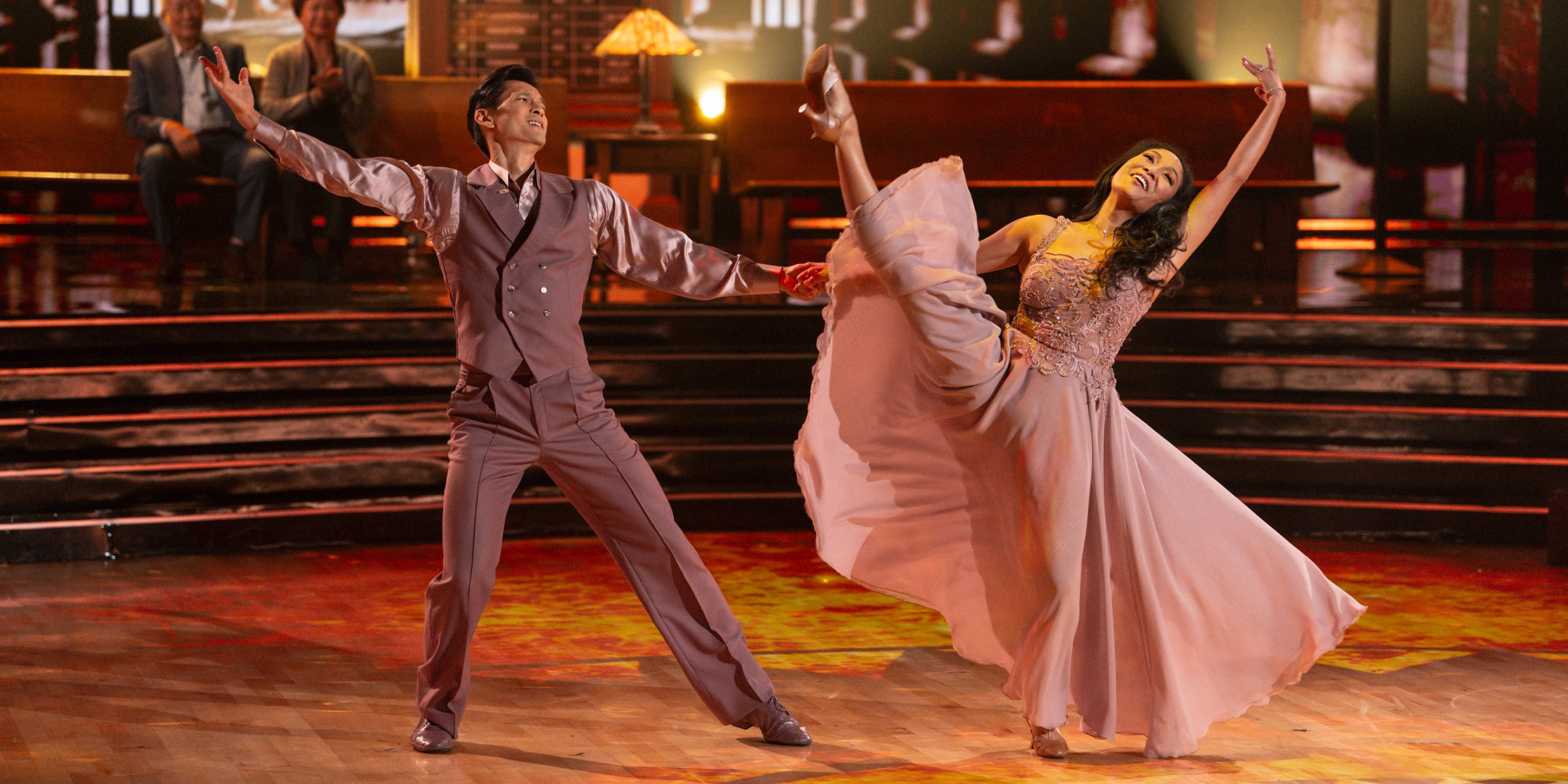 Harry Shum Jr. and his wife, Shelby Rabara, perform in mauve evening-style costumes, holding hands as Shum Jr. steps out and Rabara leans back with her inside leg in a high battement.